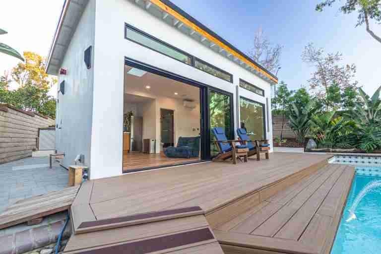 Modern backyard pool house with large glass doors and wooden deck. Huntington Beach CA