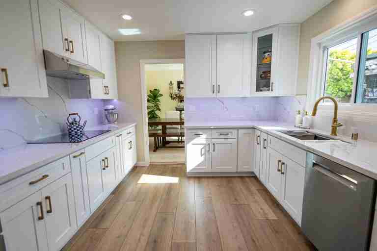 Modern white kitchen with wooden flooring, ample natural light, and sleek cabinetry in Fullerton, CA.