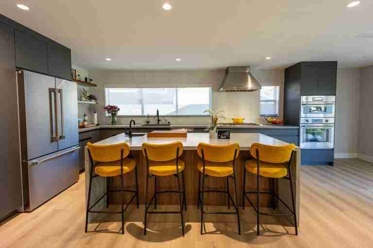 Modern kitchen featuring a large island with five yellow bar stools and sleek appliances. Fountain Valley CA