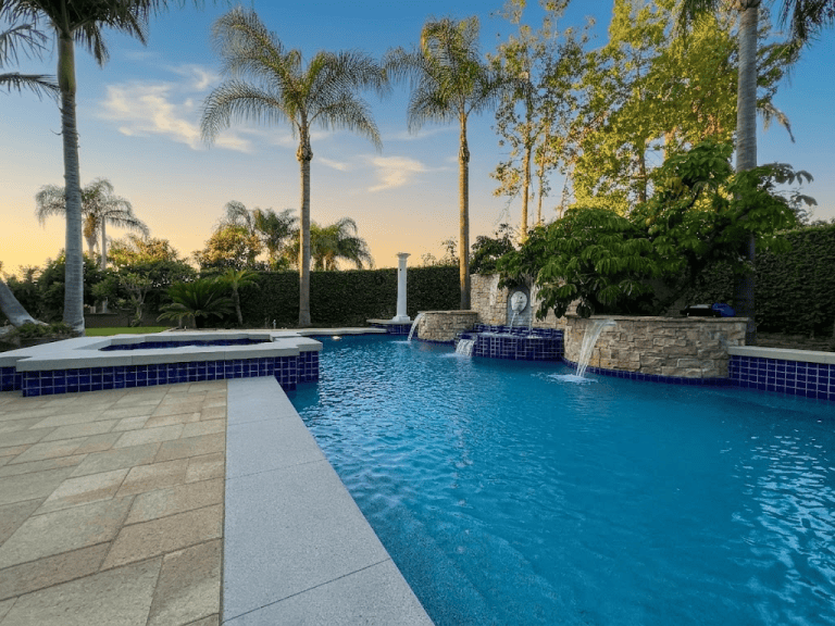 Beautiful backyard pool with waterfall, surrounded by palm trees and lush greenery in Anaheim, CA.