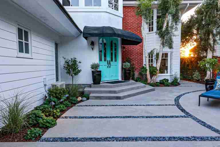 Stylish front yard with concrete pathway, lush plants, and a bright turquoise door at sunset. Buena Park, CA